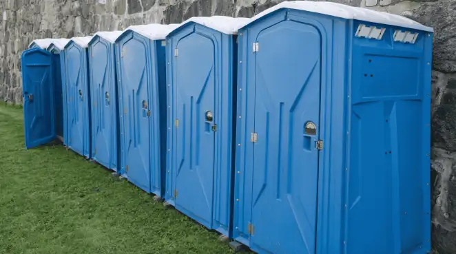 Row of blue portable toilets lined up on grass against a stone wall for event sanitation in Oklahoma City, OK